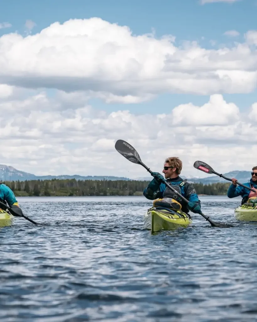 Three people in yellow kayaks and calm lake water in Grand Teton National Park.