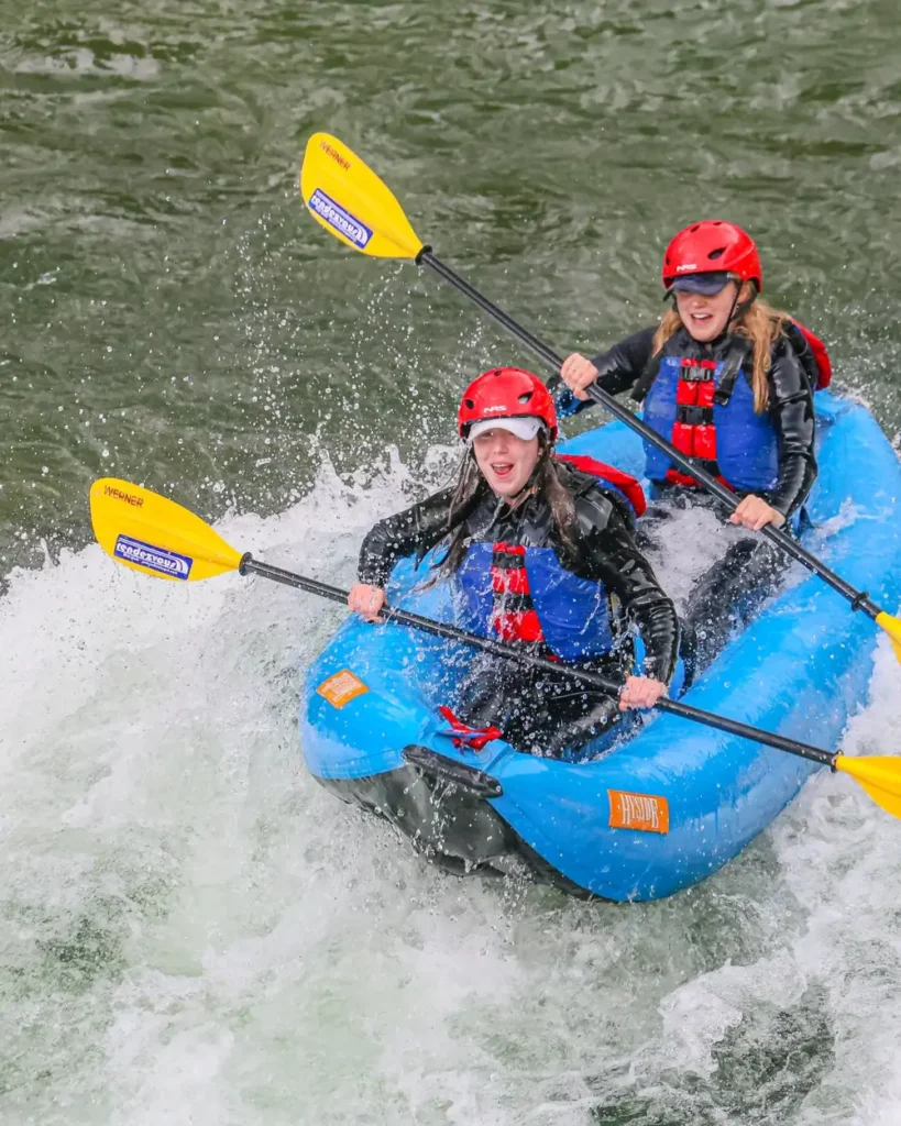 Two people in a blue inflatable kayak or raft and both wearing red helmets in Grand Teton National Park.