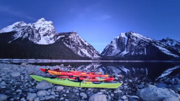 Three kayaks on rocky shore and one yellow-green kayak in foreground in Grand Teton National Park.