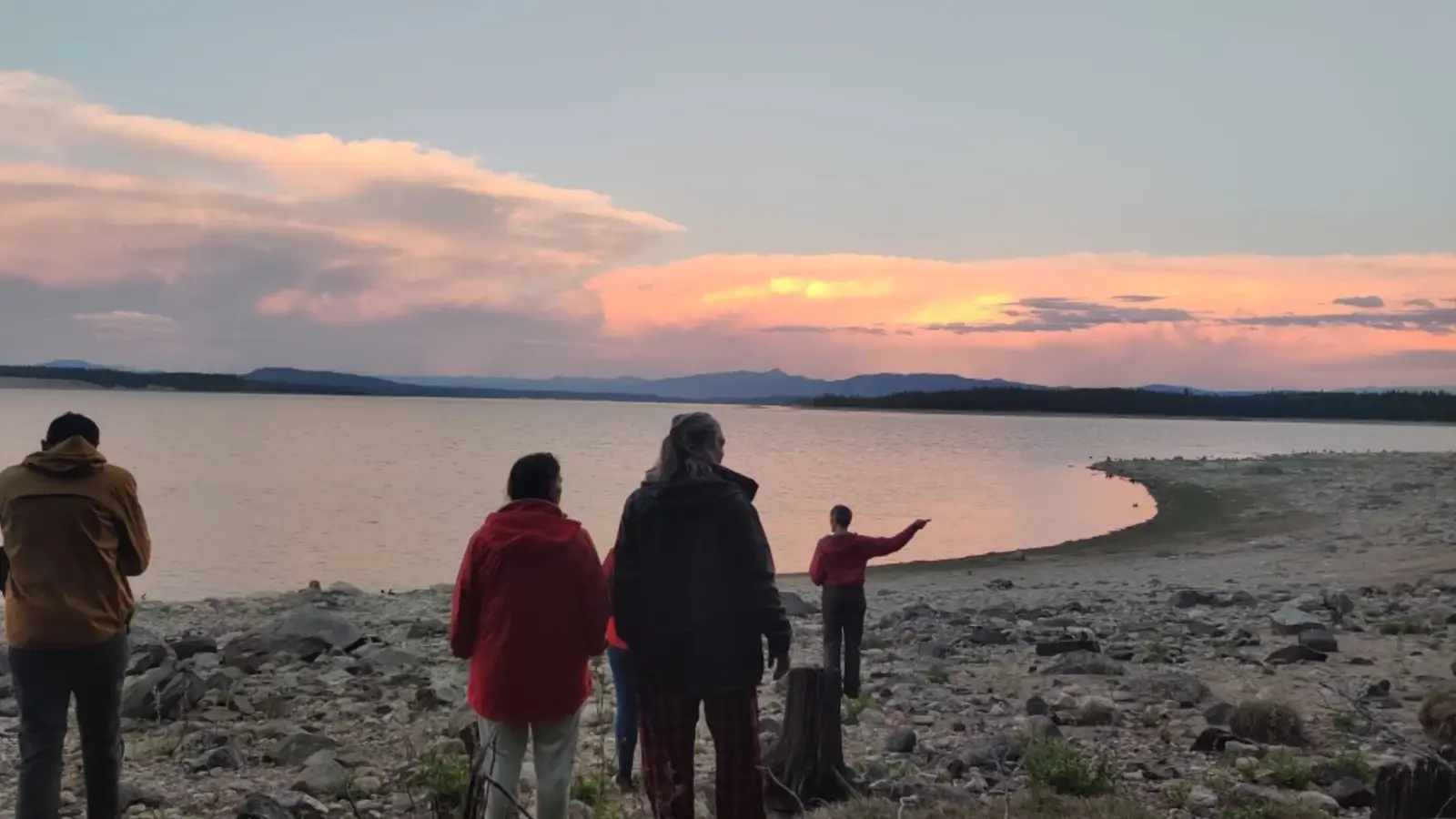 Four people standing on rocky shoreline and large lake or reservoir with calm water in Snake River.