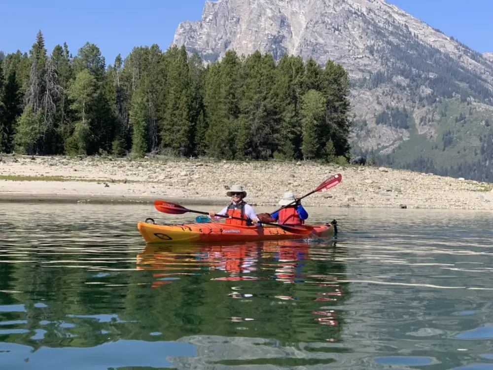 Two people in orange tandem kayak and calm green water with reflections in Snake River.
