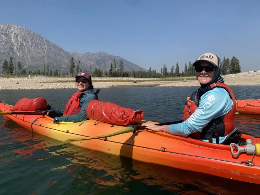Two people seated in an orange inflatable boat on water and both people wearing red life jackets in Snake River.