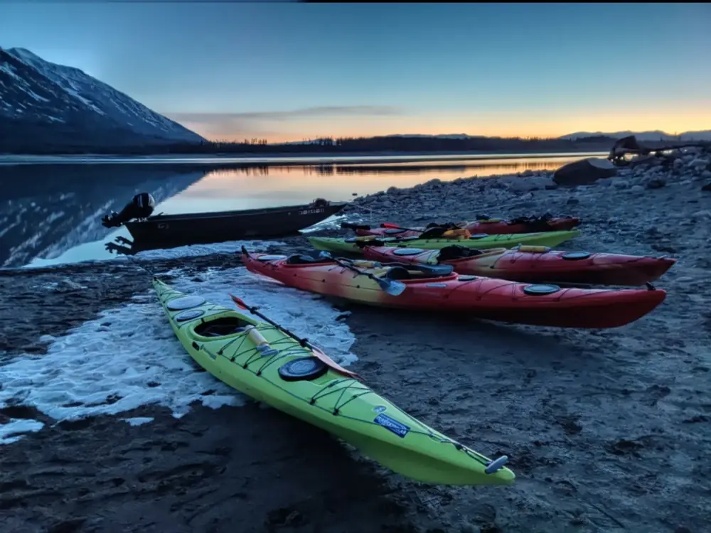 Six kayaks on rocky shoreline and two green kayaks in foreground in Grand Teton National Park.