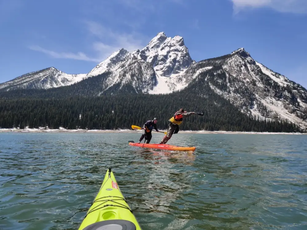Two kayaks on turquoise lake water and yellow kayak in foreground in Grand Teton National Park.