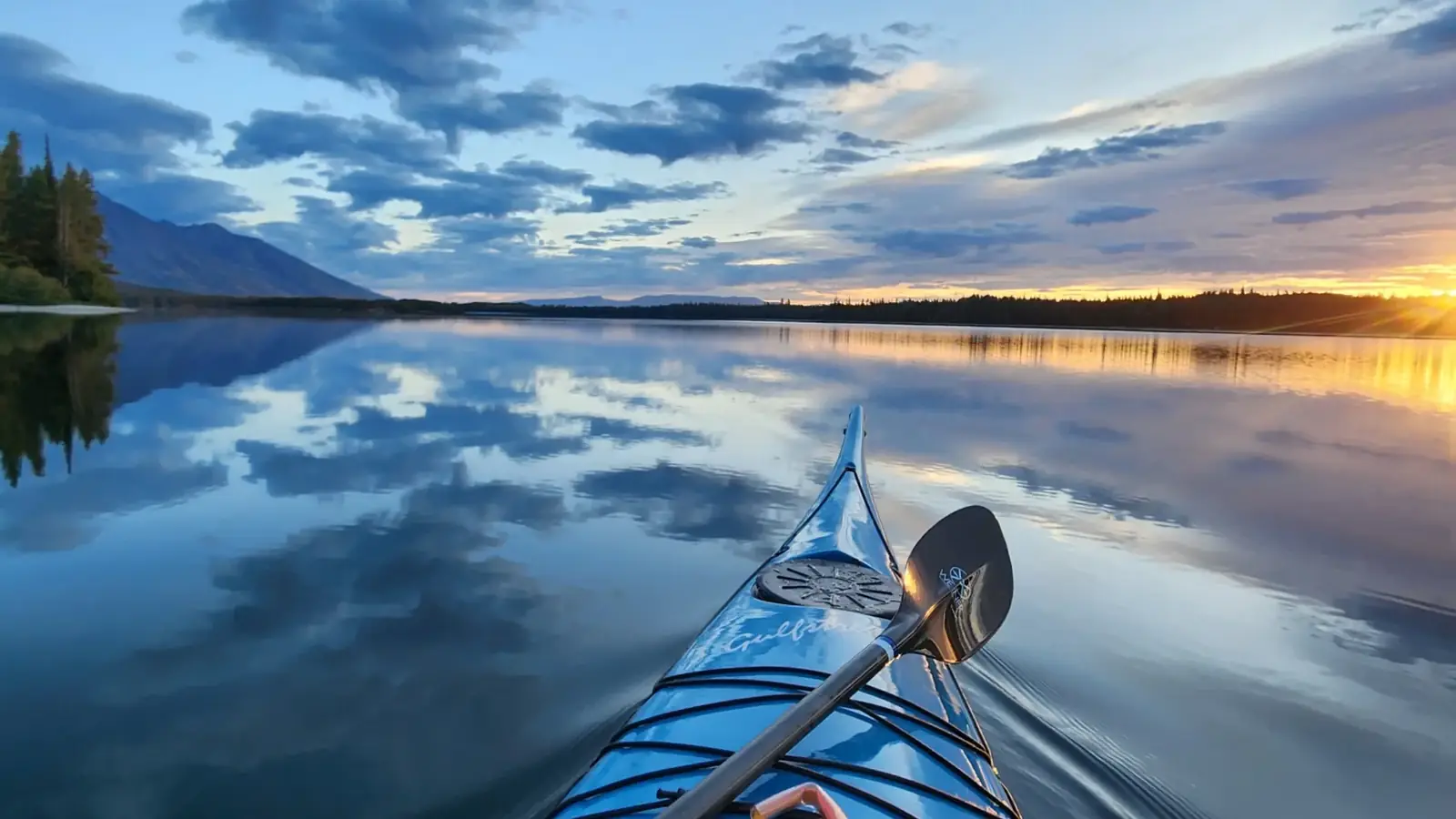 Bow of a blue kayak in the foreground and black paddle resting across the kayak in Jackson Hole.