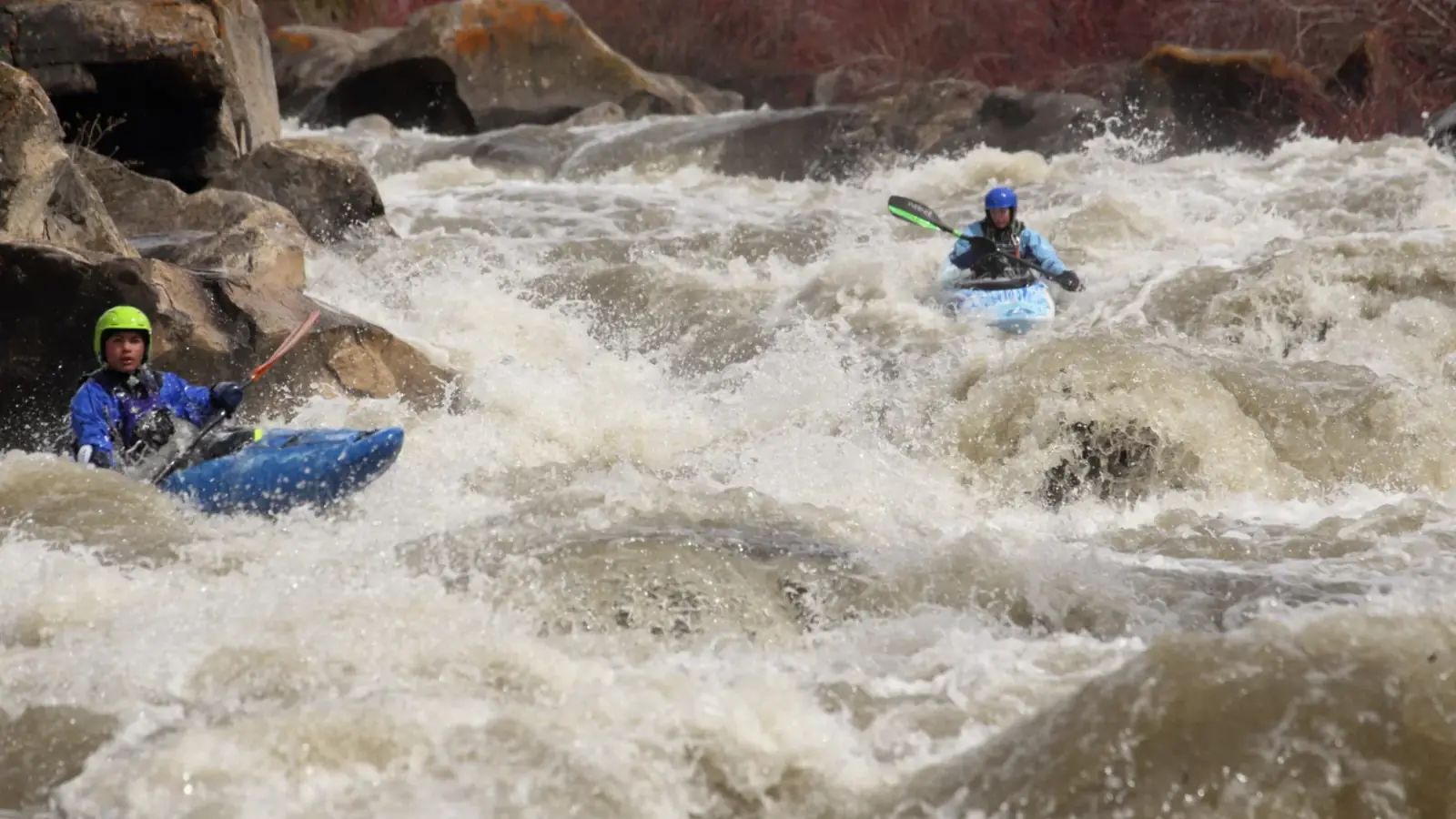 Two people in blue kayaks and each person holding a paddle in Jackson Hole.