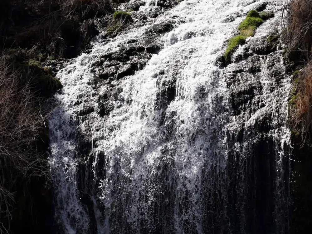 A waterfall cascading over dark rock and white, foaming water flowing down multiple rock steps in Jackson Hole.