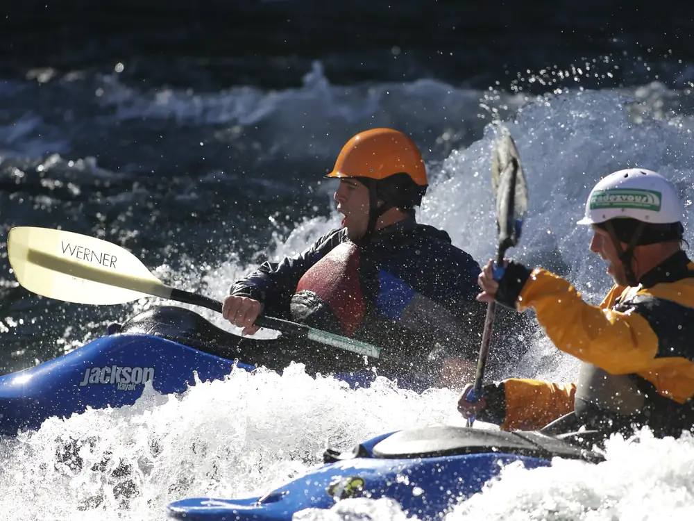 Two people in blue kayaks and whitewater river with splashing waves in Yellowstone National Park.