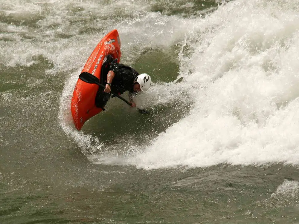 Person in orange kayak on calm water and orange or red kayak in Yellowstone National Park.