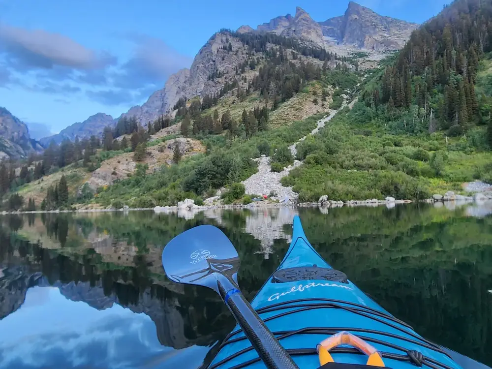 Blue kayak bow in foreground and double-bladed paddle resting across the kayak in Yellowstone National Park.