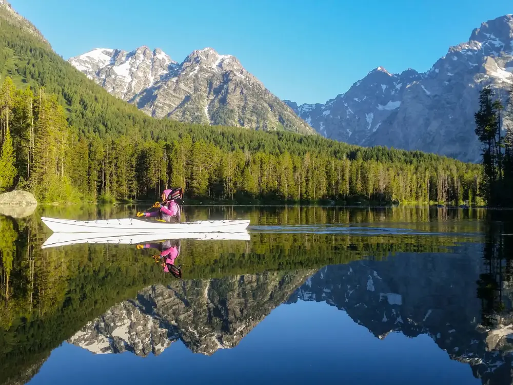 One person seated in a white kayak and person wearing a pink jacket and a black vest in Yellowstone National Park.