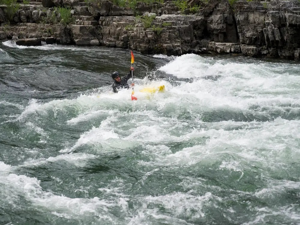 One person in a yellow kayak and kayak paddle with orange and red blade in Yellowstone National Park.