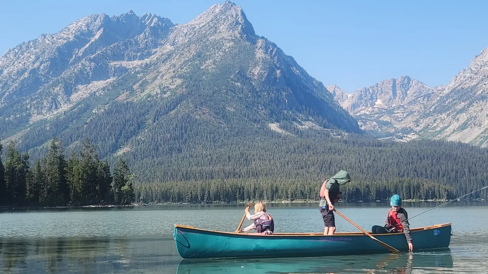 Turquoise canoe on calm lake and three people in the canoe in Jackson Hole.