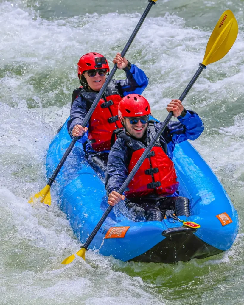 Two people in a blue inflatable raft and whitewater river with foamy rapids in Jackson Hole.