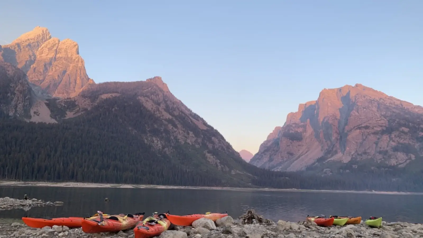 Multiple kayaks on rocky shore and orange kayaks in Grand Teton National Park.