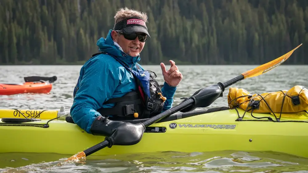 Person standing and gesturing and yellow kayak on grass in Jackson Hole.