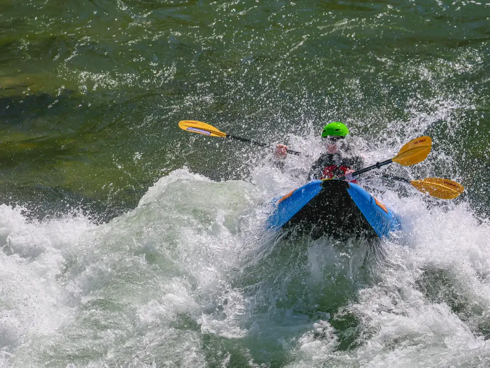 One person in a blue kayak and person wearing a bright green helmet in Jackson Hole.
