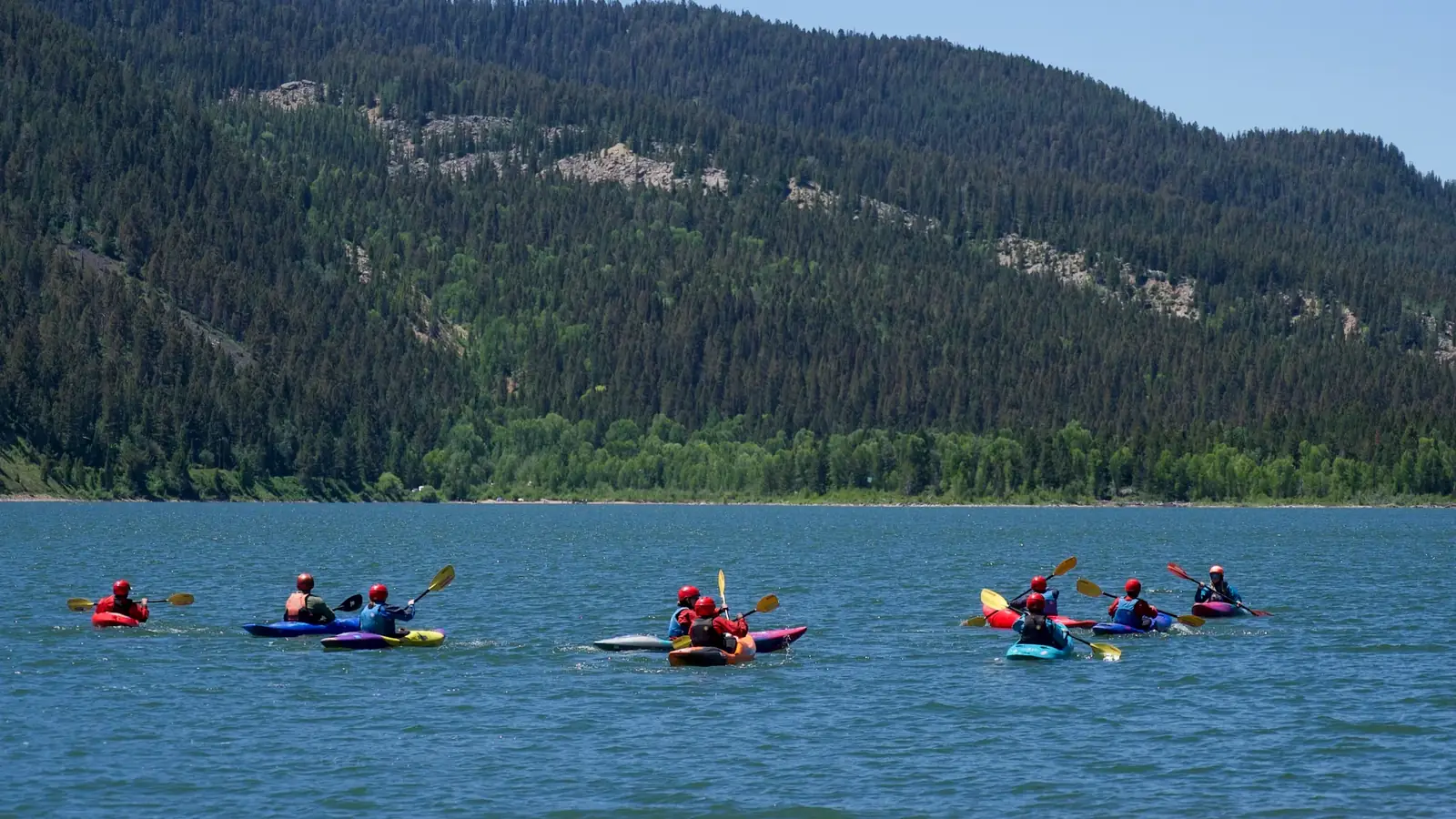Group of nine people in kayaks on calm lake water and seven kayaks total - mixture of single and tandem kayaks in Jackson Hole