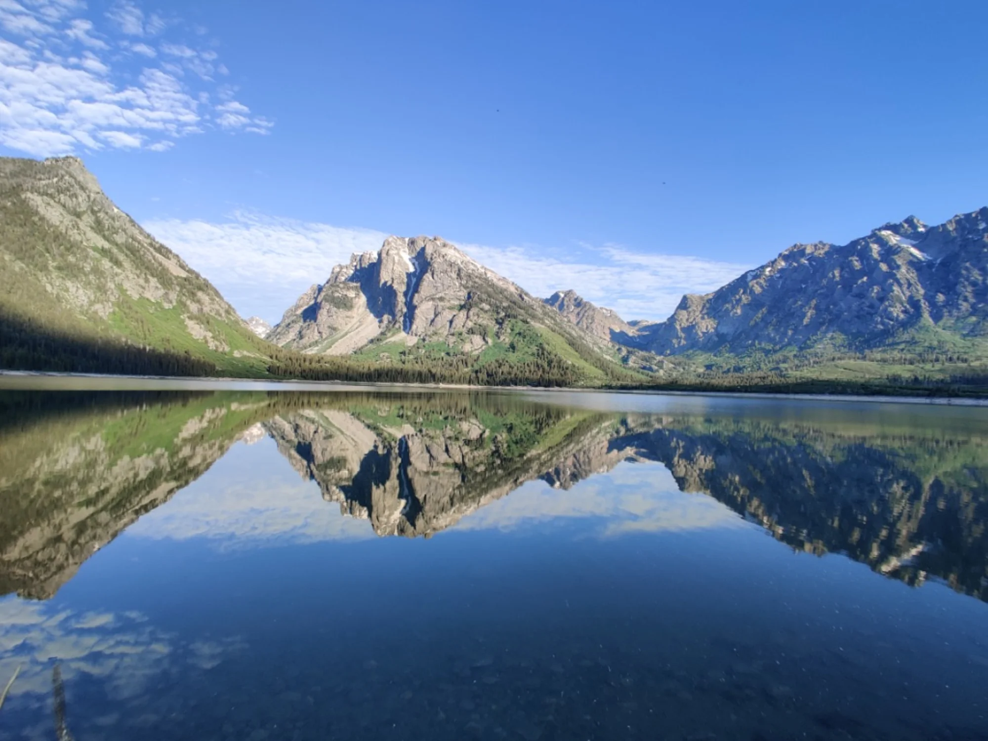 Two people in a small inflatable boat on calm water and one person wearing a light blue top and white hat in Yellowstone National Park