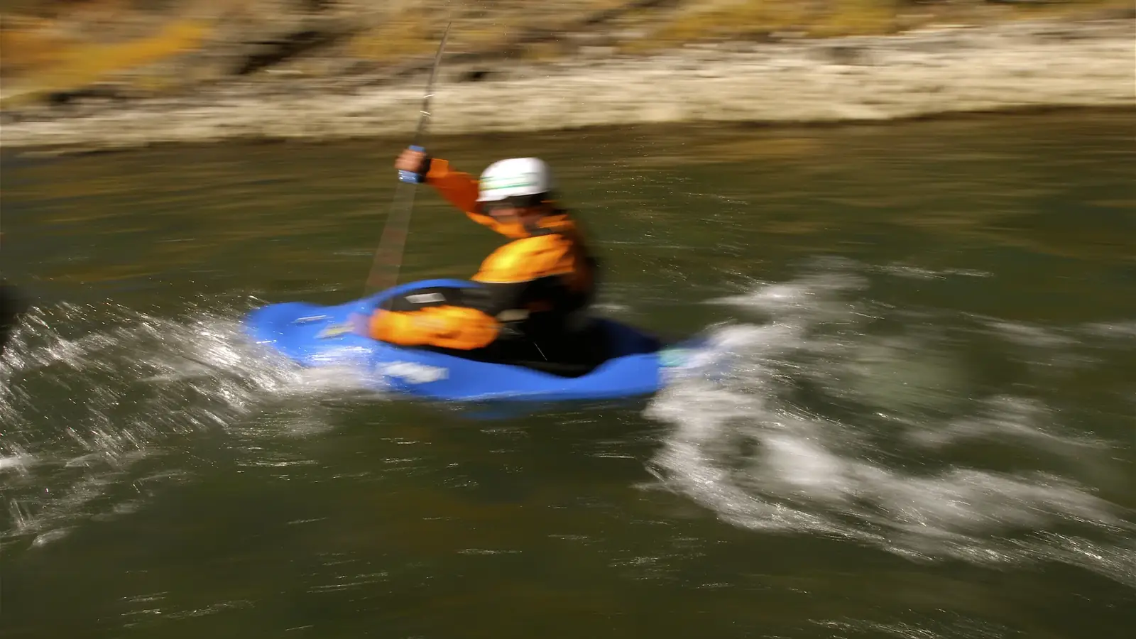 One person in a blue kayak and person wearing an orange jacket and white helmet in Jackson Hole.