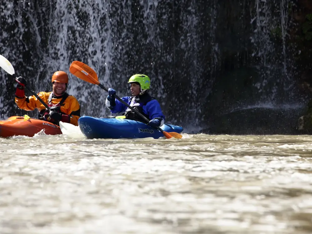 Two people in kayaks on a river and orange kayak with white paddle held by the left person in Jackson Hole.