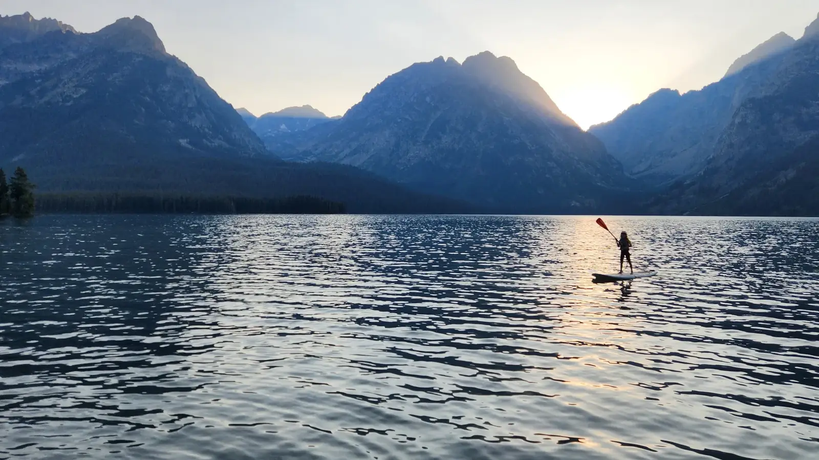One person standing on a paddleboard and person holding a single-blade paddle in Slide Lake.