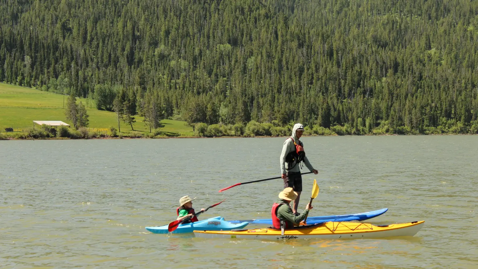 Three people on two kayaks on calm lake water and adult standing on blue paddleboard or kayak in background in Slide Lake