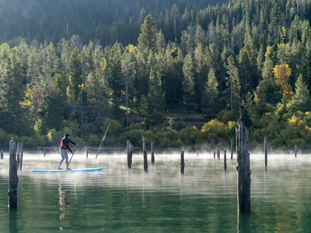 One person standing on a blue stand-up paddleboard and person holding a paddle in Slide Lake.