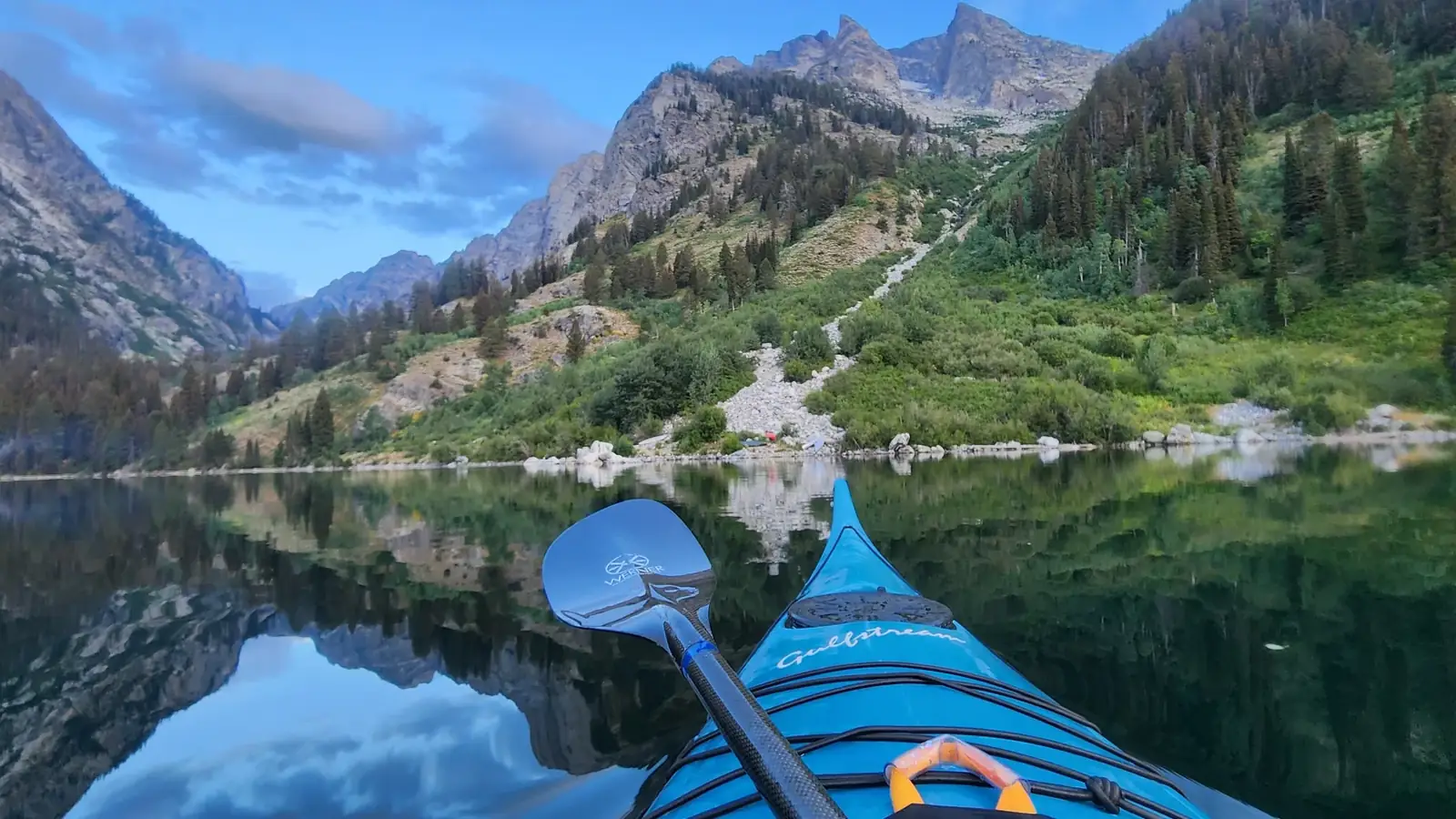 Blue kayak bow in foreground and double-bladed paddle resting across the kayak in Jackson Hole.