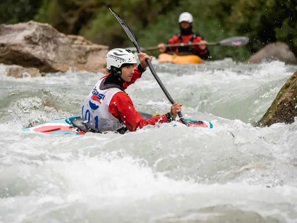 Two people in kayaks and foreground kayaker wearing a white helmet and red jacket in Jackson Hole.