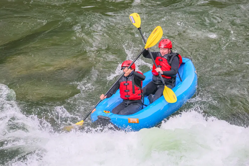 Two people in a blue inflatable kayak and both wearing red helmets in Snake River.