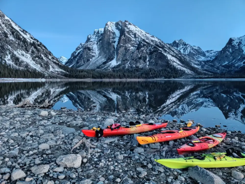 Three kayaks on rocky shoreline and one red kayak in Yellowstone National Park.