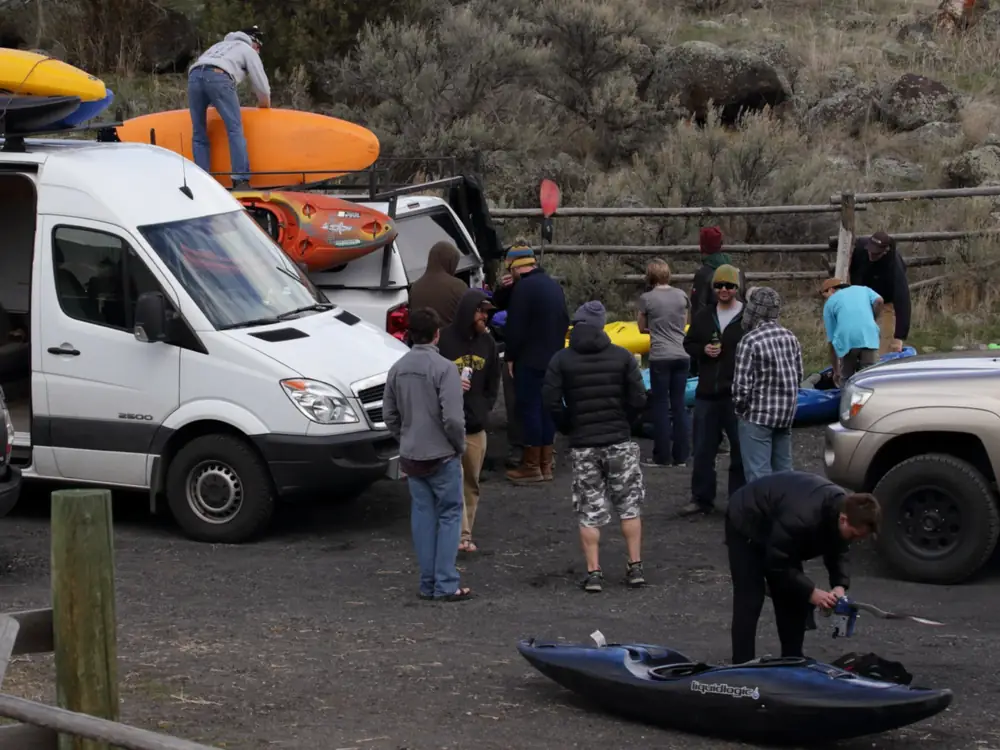 Group of people standing in a gravel parking area and white cargo van with kayaks on the roof in Jackson Hole.