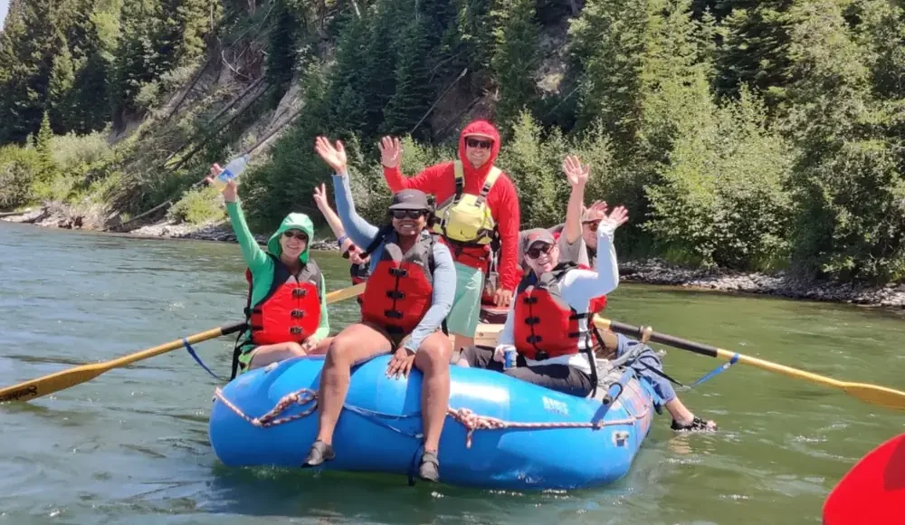 Single kayaker in red or orange kayak and rocky riverbed with scattered boulders in Snake River.