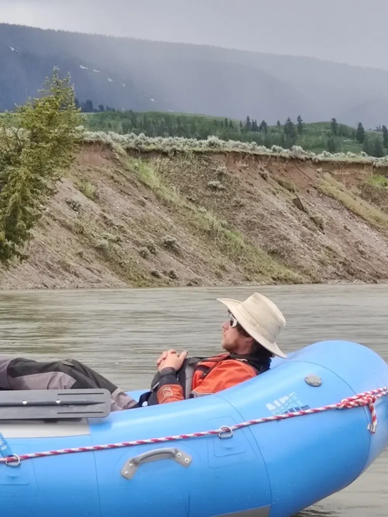 One person in blue inflatable raft and person wearing tan or beige sun hat in Snake River.