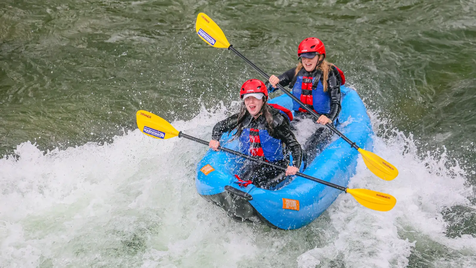 Two people in a blue inflatable kayak or raft and both wearing red helmets in Snake River.