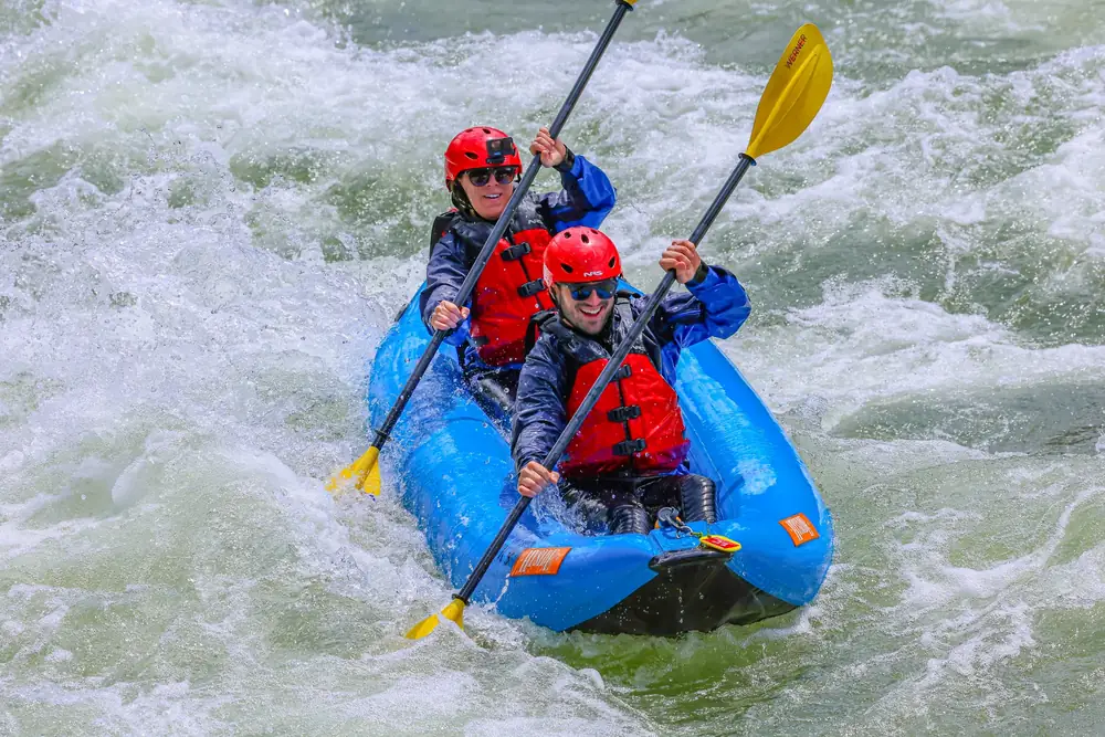 Two people in a blue inflatable raft and whitewater river with foamy rapids in Snake River.
