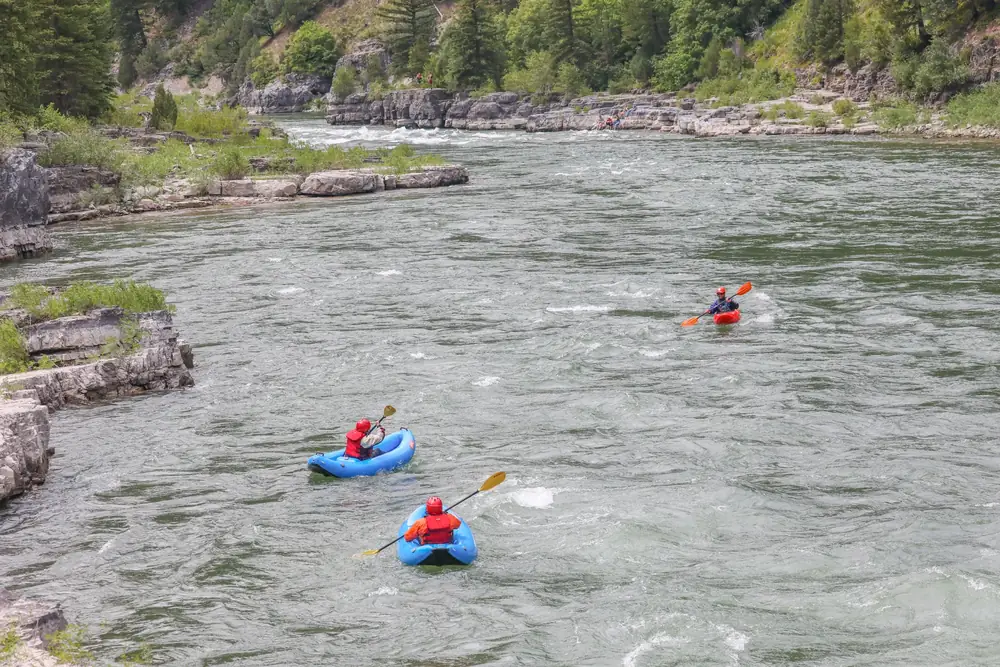 Three people in inflatable kayaks on clear river water and two blue inflatable kayaks in foreground in Snake River.