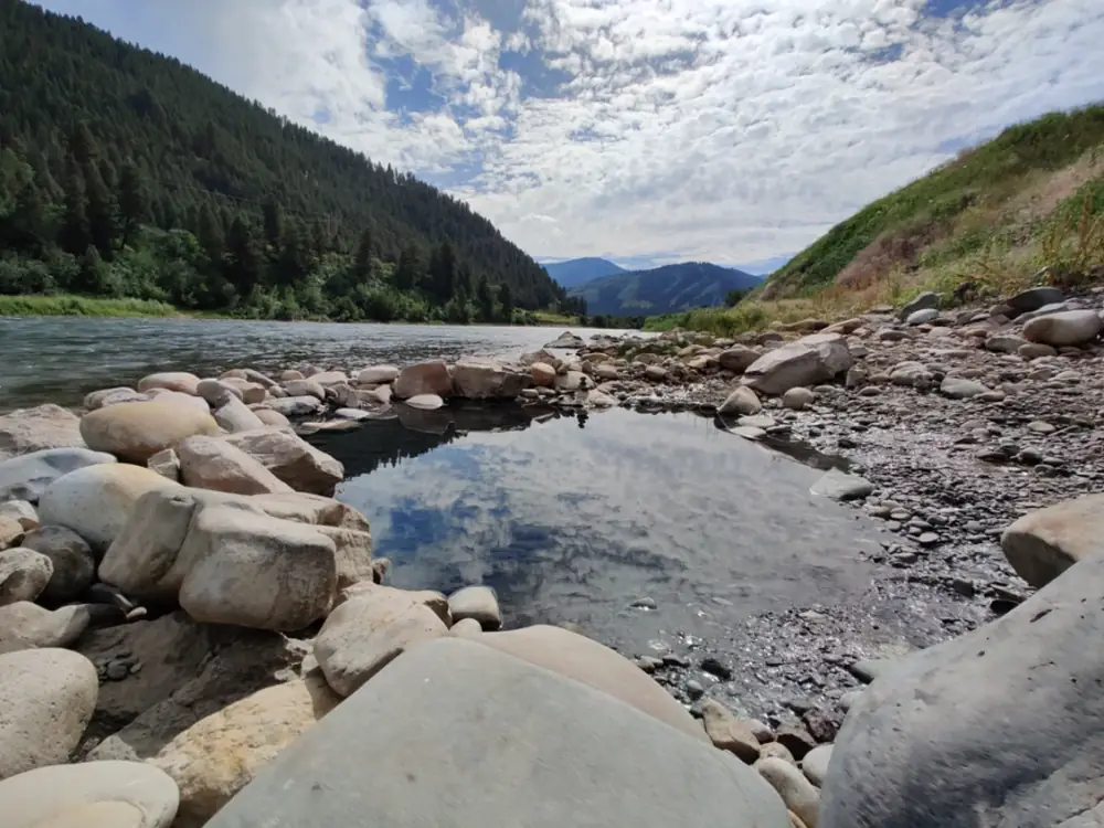 Person in red kayak on river and rocky riverbank with large boulders in Snake River.