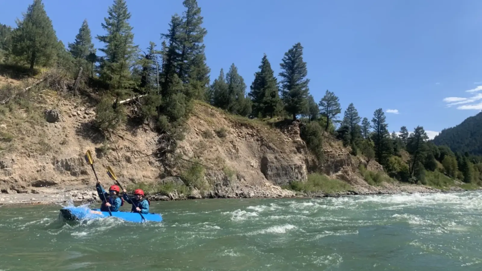 Two people in a blue inflatable raft and both wearing red helmets in Snake River.