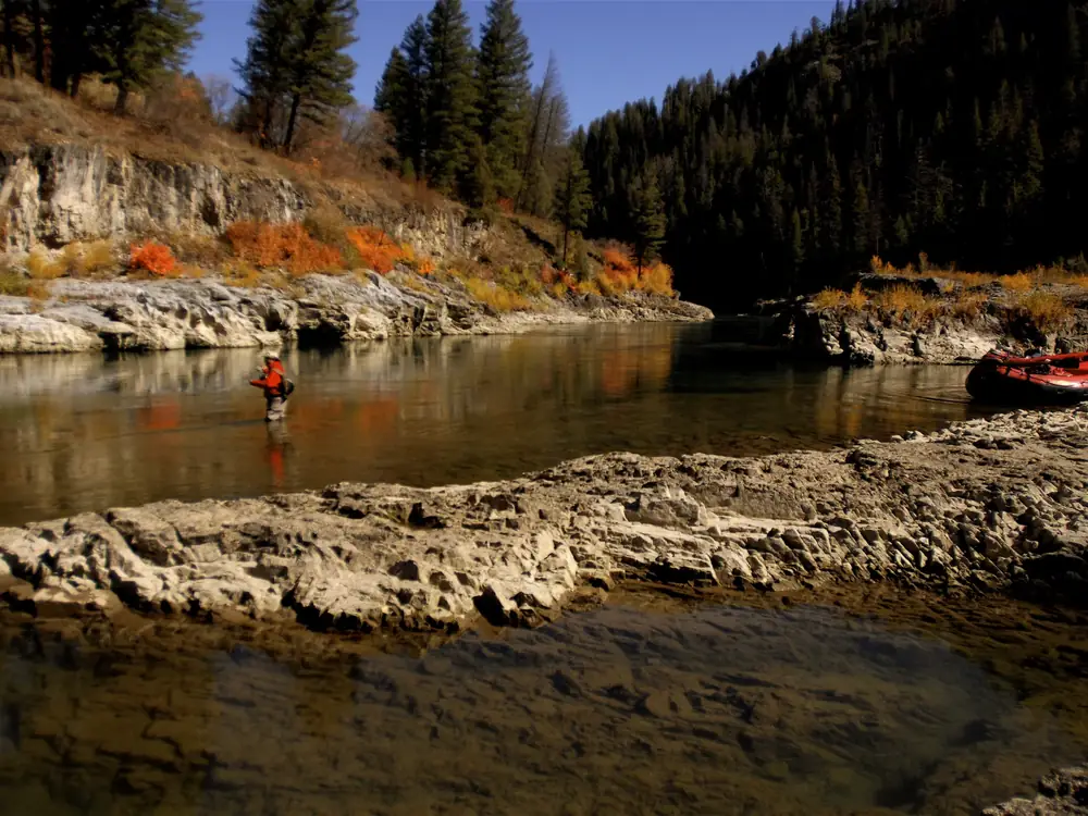 Rocky riverbank in the foreground and clear, shallow river with visible riverbed in Jackson Hole.
