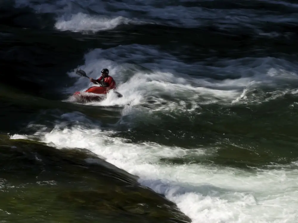 Person in red or pink kayak in center and person in yellow kayak in background in Jackson Hole.
