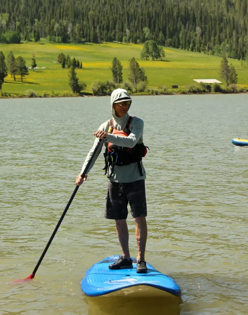 One person standing on a blue stand-up paddleboard holding a paddle and red paddle blade in the water in Jackson Hole.