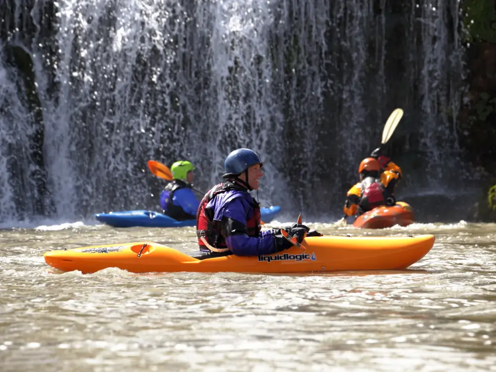 Three people in kayaks and orange kayak in the foreground in Jackson Hole.