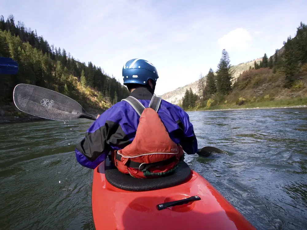 Person in red kayak and blue helmet in Snake River.