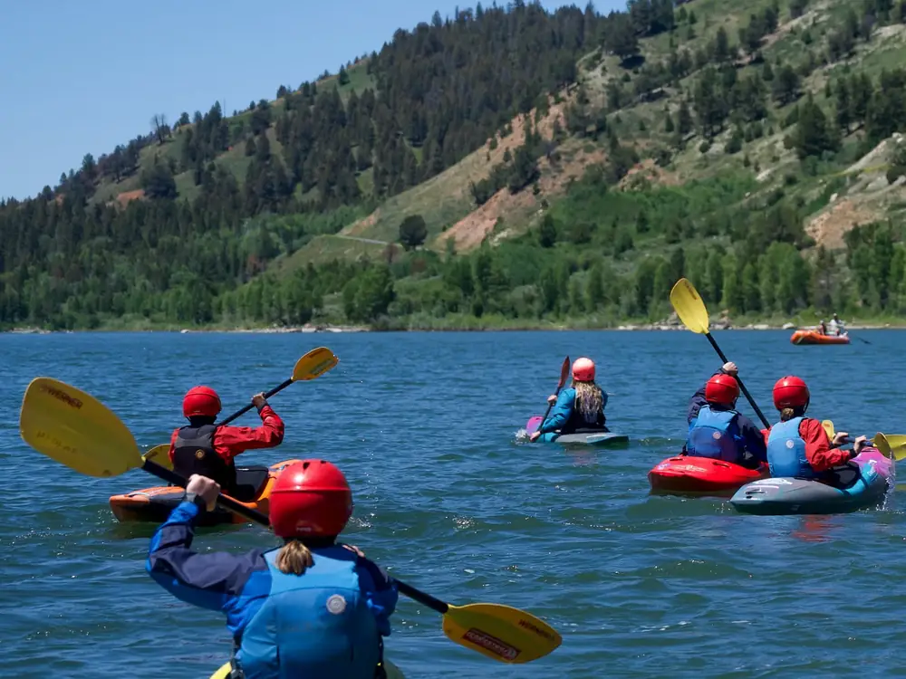 Multiple people in kayaks on calm blue water and red and yellow inflatable kayaks in Snake River.
