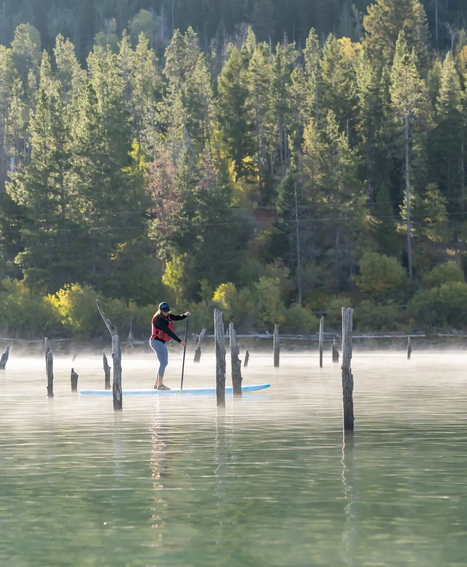 One person standing on a stand-up paddleboard and person holding a paddle in Snake River.