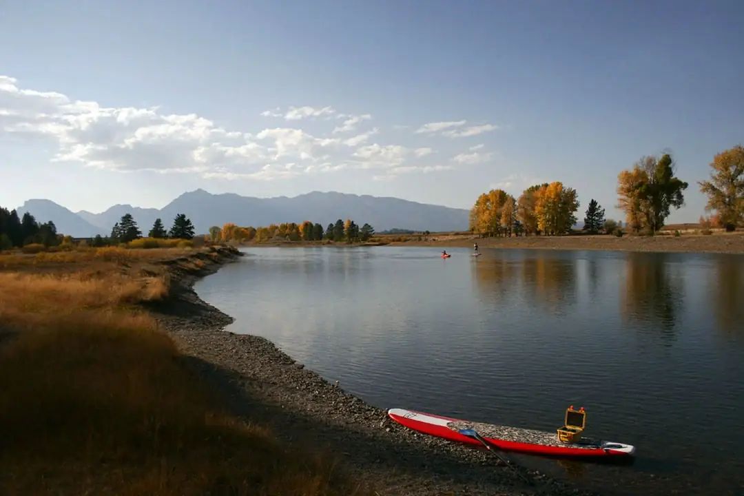 Bare feet and lower legs and red board with textured deck pad in Snake River.