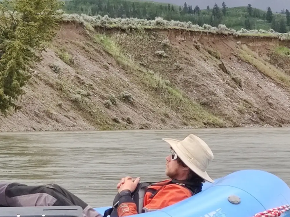 One person in blue inflatable raft and person wearing tan or beige sun hat in Snake River.