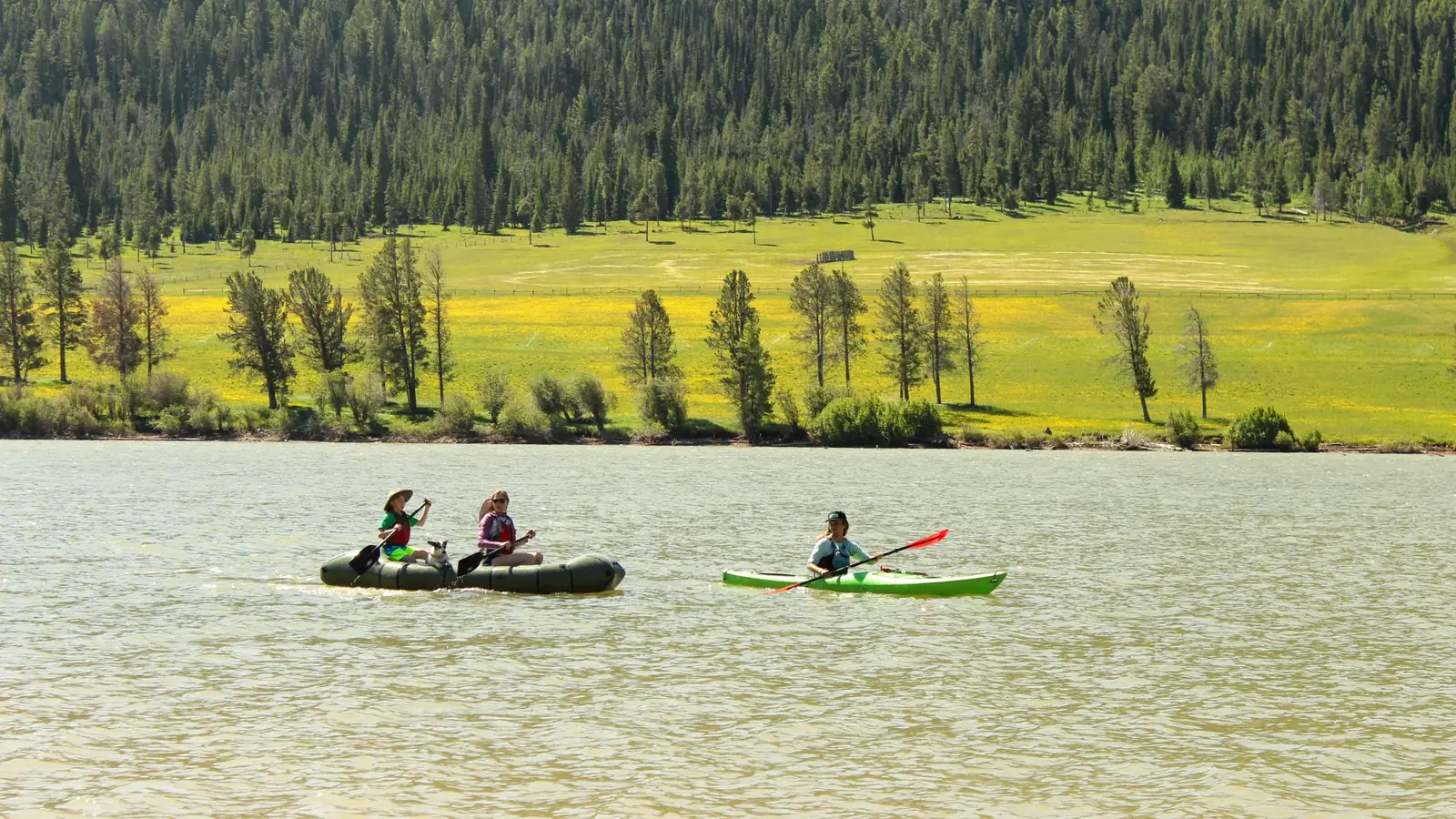 Calm body of water with small ripples and two people in a dark inflatable raft in Slide Lake.